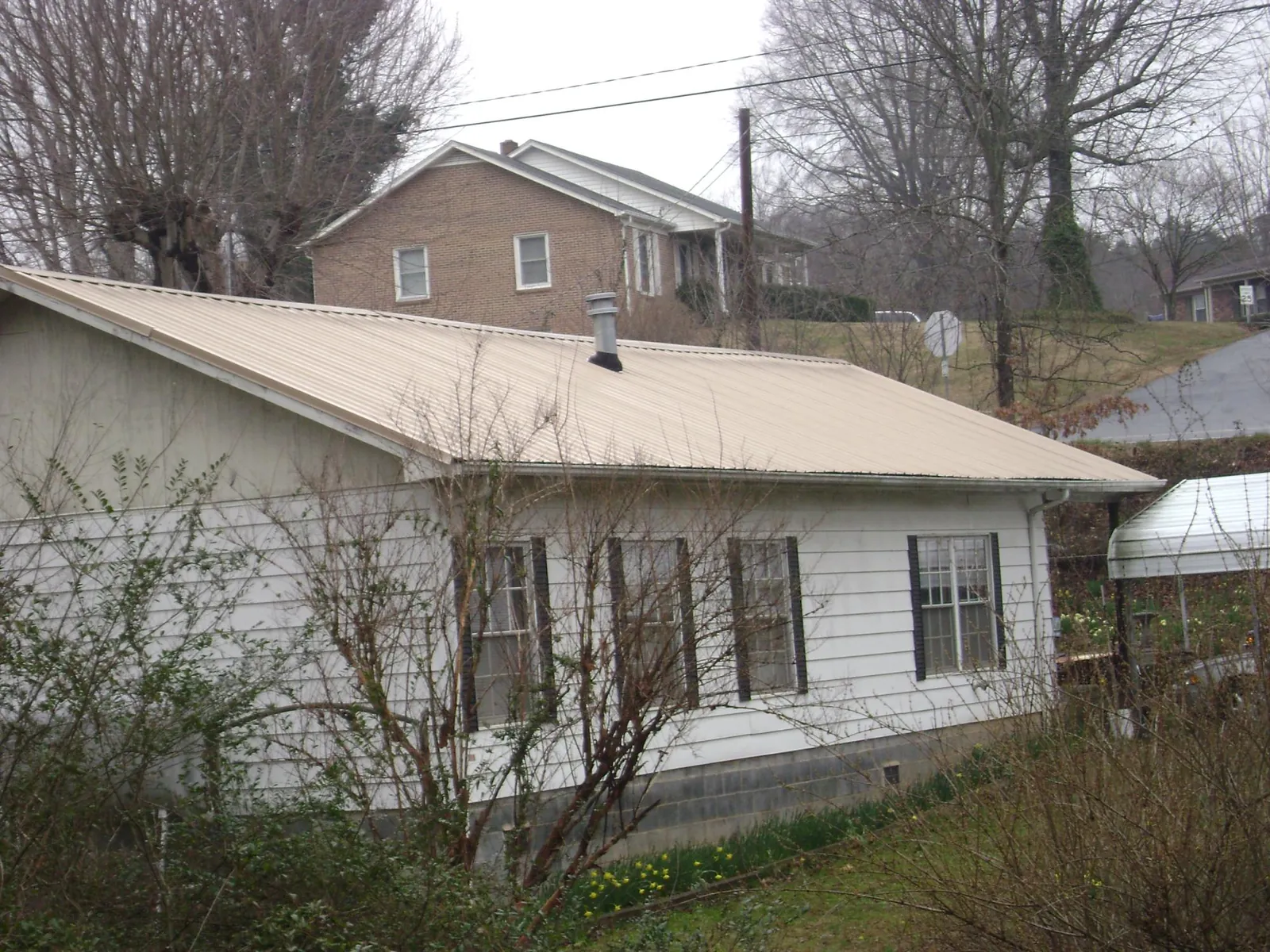 Tan metal roof on a white sided house set into a hillside — Commercial Roofing by Roofing Brothers in Ortonville